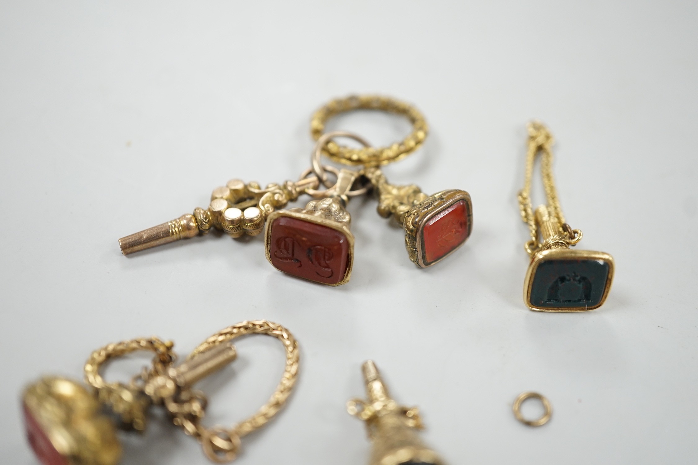 Two 19th century yellow metal overlaid and bloodstone set watch key fobs, one of funnel form, 21mm, a similar gold plated and carnelian set watch key fob, two other fob seals and a watch key on chain.